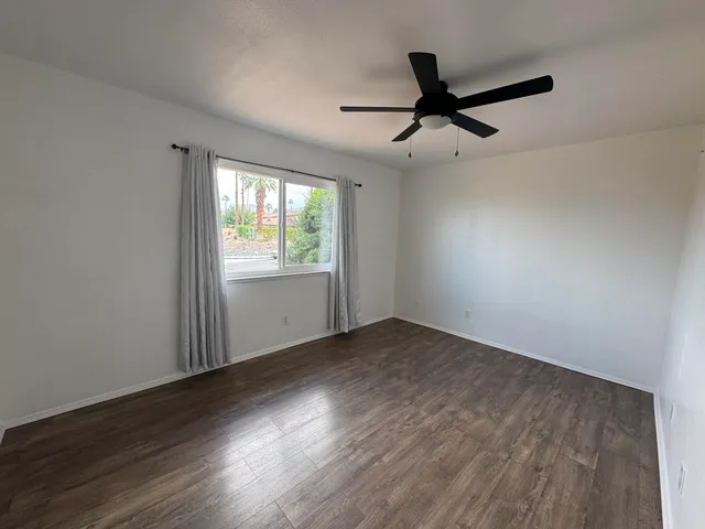 an empty room with wooden floor fan and windows