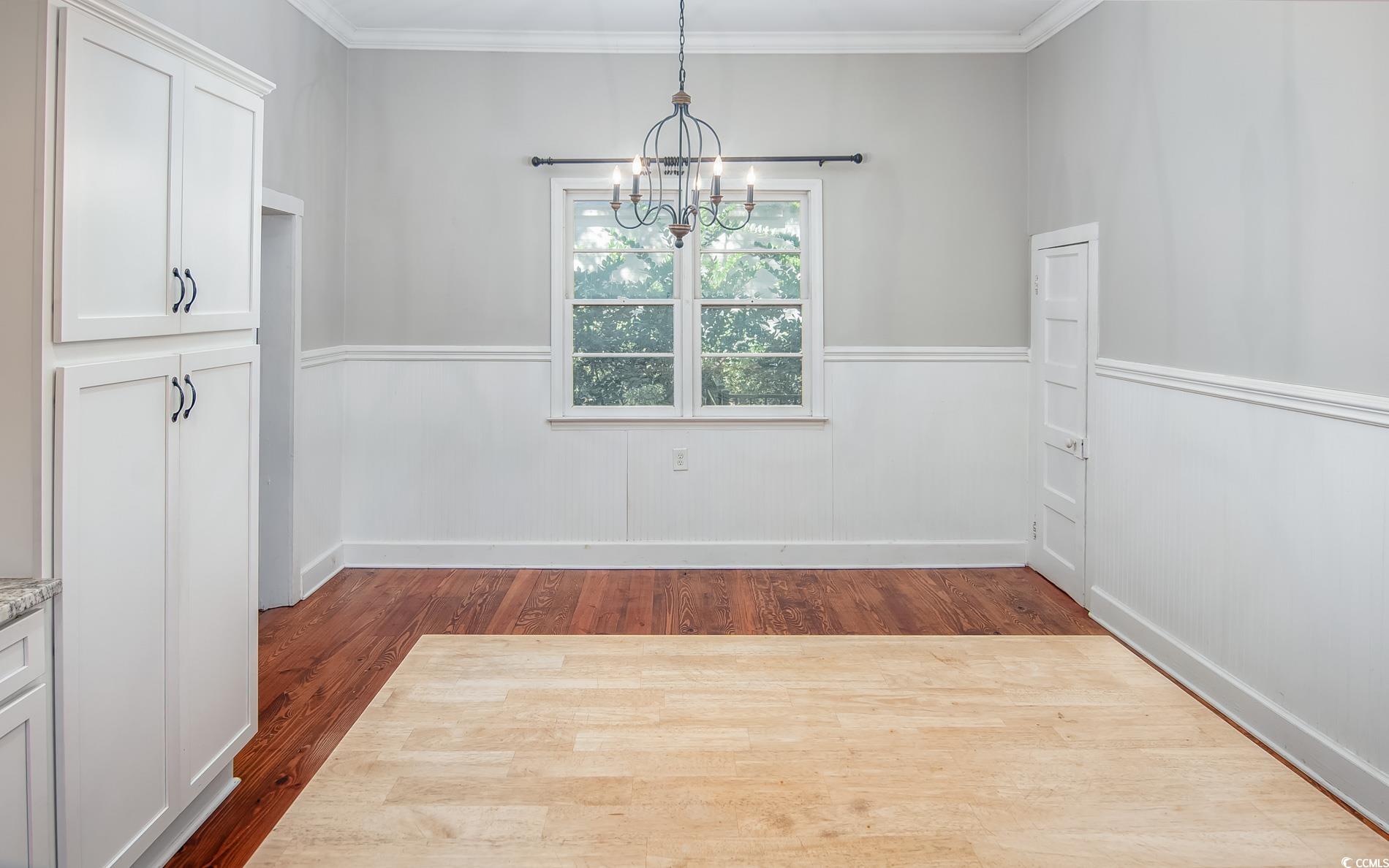 524 Highmarket Street Georgetown, SC 29440 - Photo 10 of 27 Unfurnished dining area with dark wood-style floors, a wainscoted wall, ornamental molding, and a chandelier