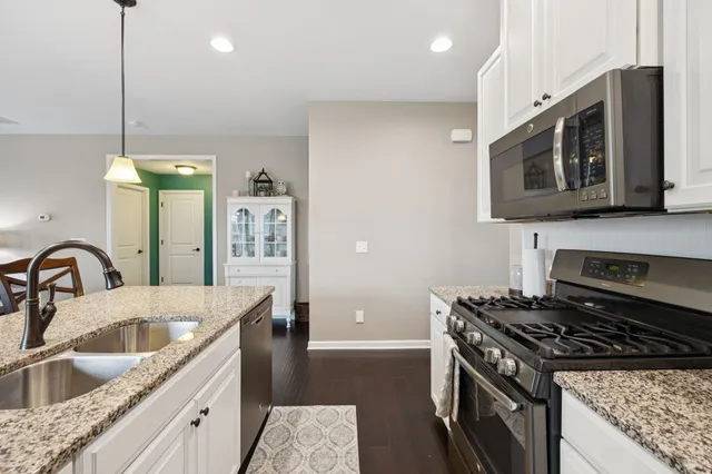 a kitchen with stainless steel appliances kitchen island granite countertop a stove a refrigerator a kitchen island a dining table and chairs with wooden floor