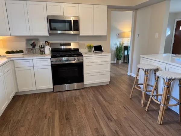 a kitchen with granite countertop wooden floors stainless steel appliances and white cabinets