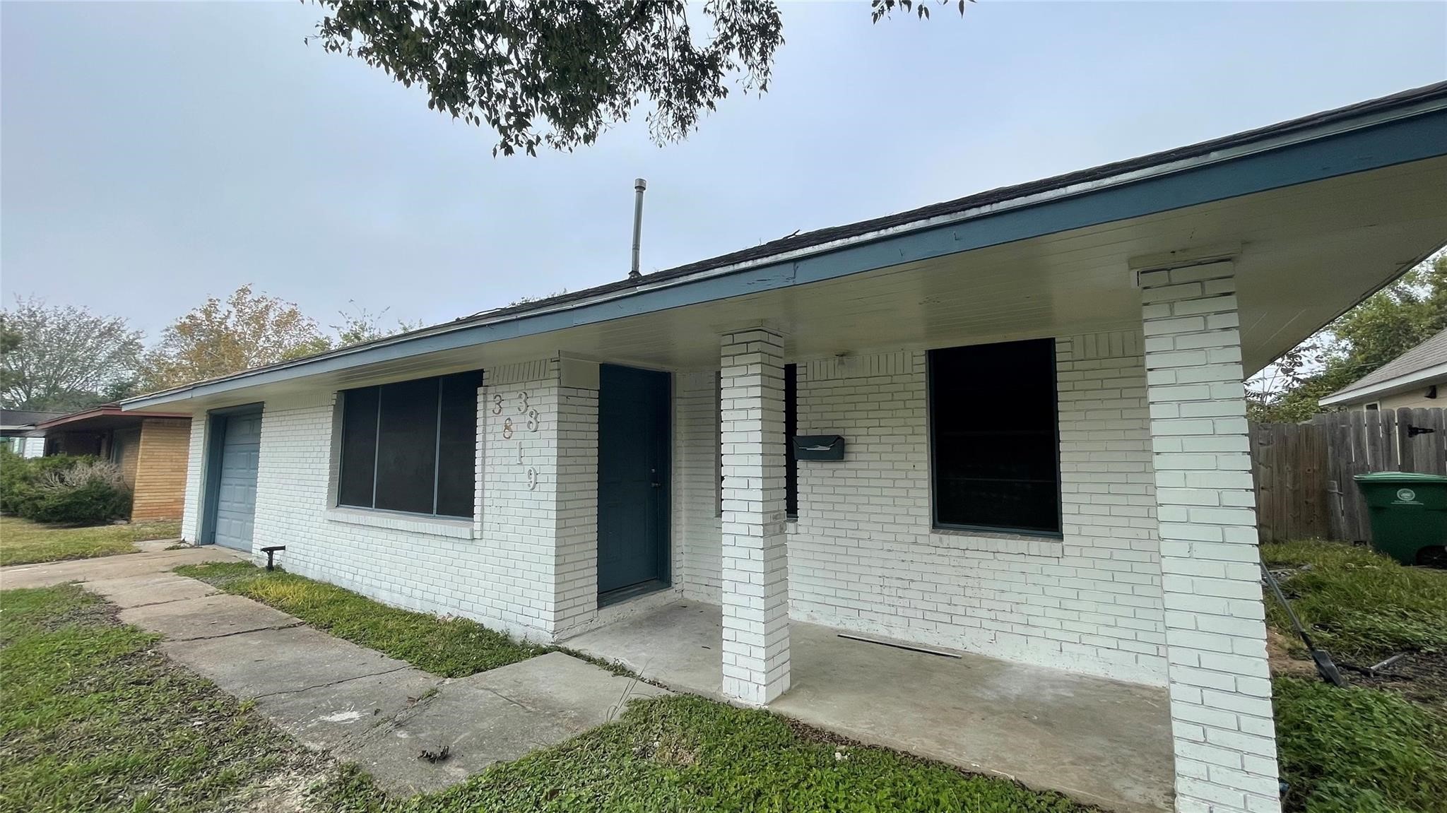 This single-story home offering a white brick exterior and a covered front porch. The house features a single garage and a small front yard with a paved walkway. The design is simple and functional, offering potential for personalization.
