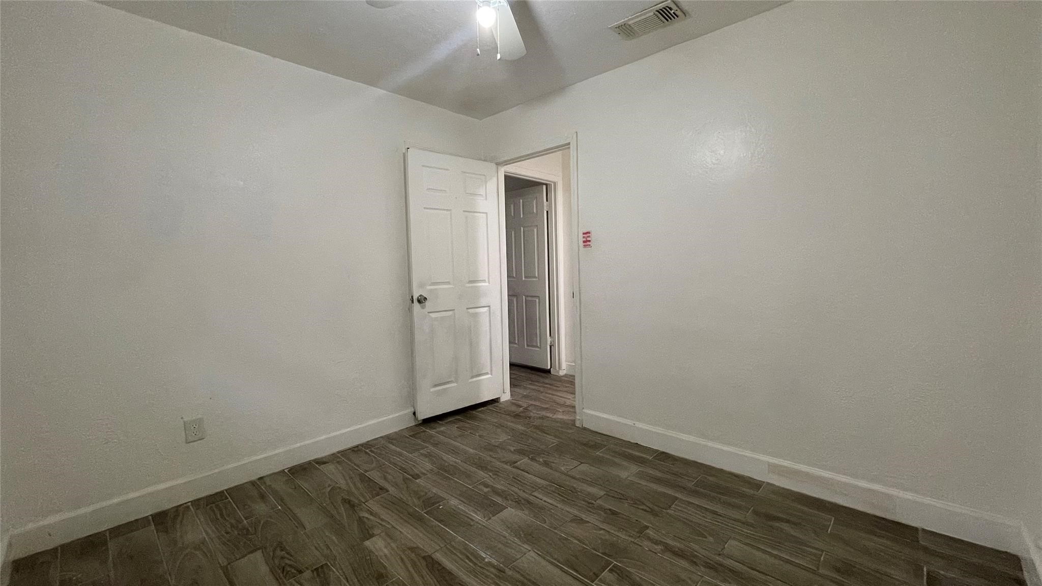 3819 Botany Lane Houston, TX 77047 - Photo 3 of 7 This bedroom features neutral paint and wood-look tile flooring, offering a modern aesthetic. It includes a door leading to an adjacent hallway or room, with a ceiling fan for added comfort.