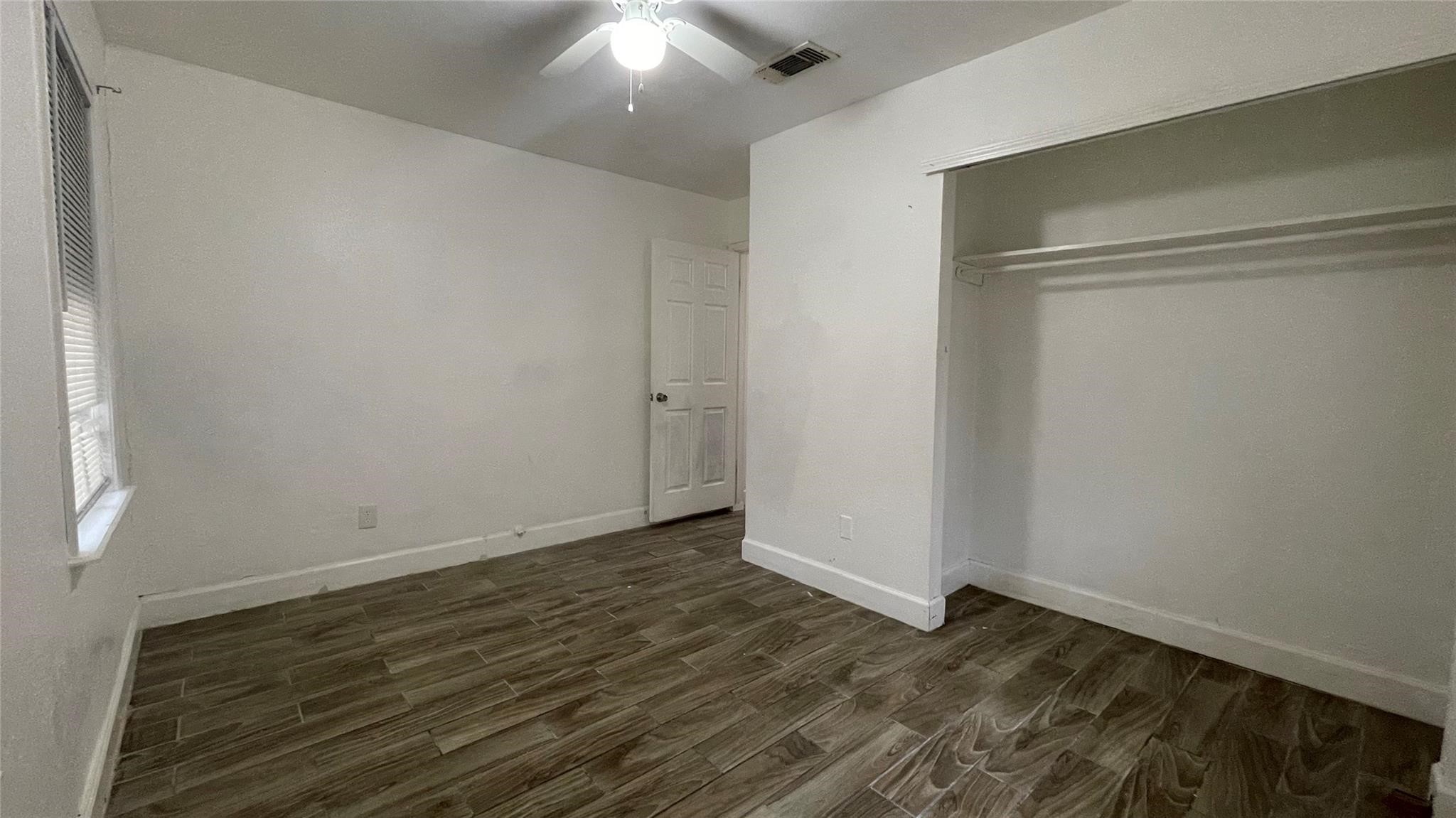 3819 Botany Lane Houston, TX 77047 - Photo 4 of 7 This room features neutral paint walls, wood-look flooring, a ceiling fan, a window for natural light, and an open closet space.