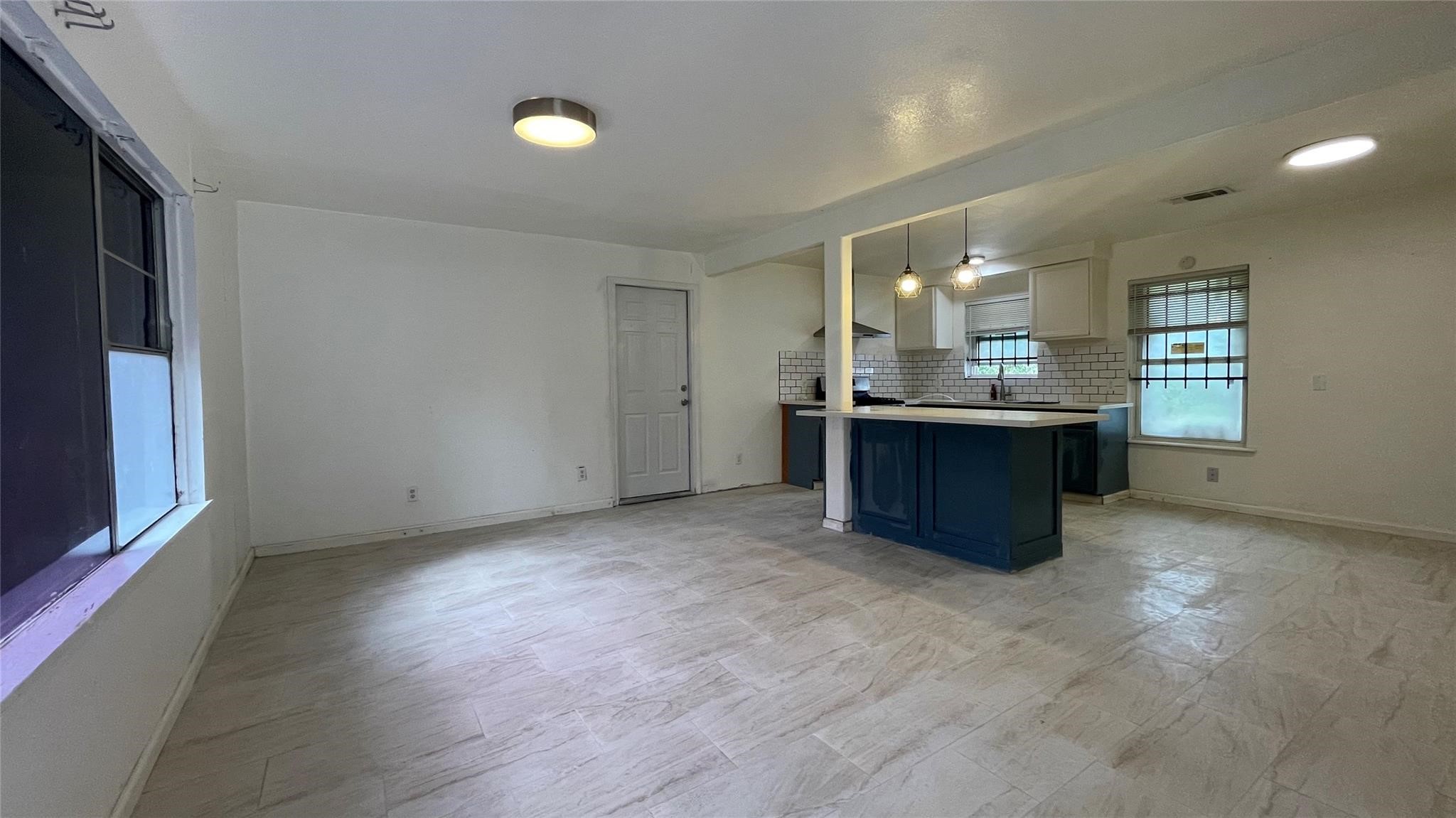 3819 Botany Lane Houston, TX 77047 - Photo 5 of 7 This photo showcases a bright, open-concept living area with modern tile flooring and ample natural light. The kitchen features a stylish island, pendant lighting, and a contemporary backsplash, creating a welcoming space for dining and entertaining.