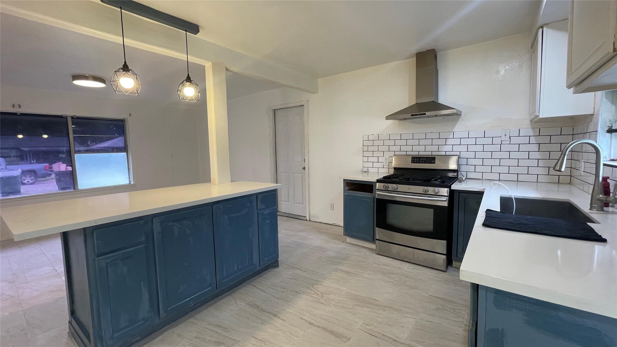 3819 Botany Lane Houston, TX 77047 - Photo 7 of 7 Modern kitchen with sleek design, featuring blue cabinetry, stainless steel appliances, and a stylish subway tile backsplash. The large island with pendant lighting provides ample workspace and seating.