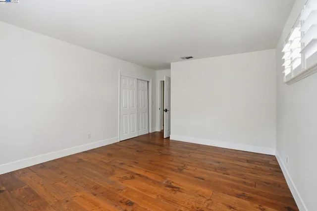 a view of an empty room with wooden floor and a bathroom