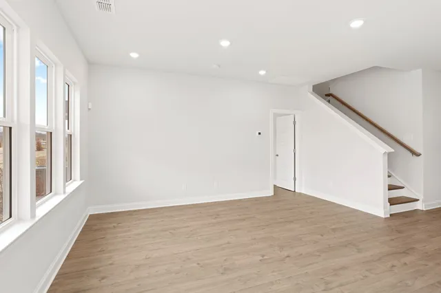 a view of an empty room with wooden floor and stairs