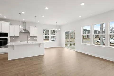a large white kitchen with kitchen island a large window wooden floor and stainless steel appliances