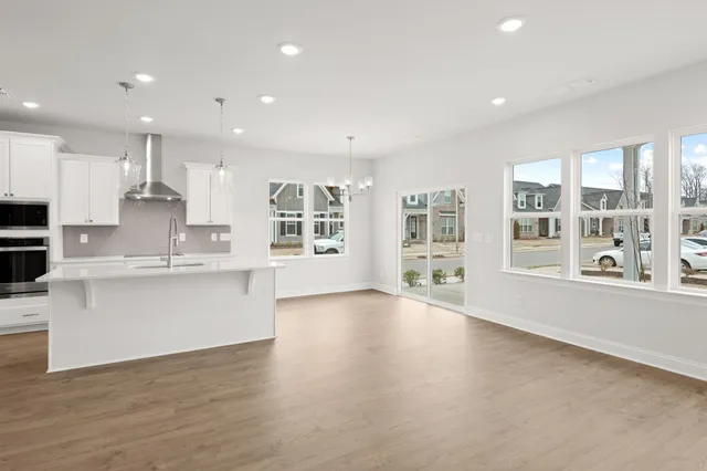 a large white kitchen with kitchen island a large window wooden floor and stainless steel appliances