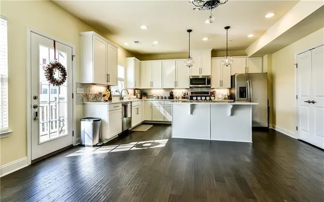 a kitchen with stainless steel appliances granite countertop a refrigerator a stove a sink and white cabinets with wooden floor