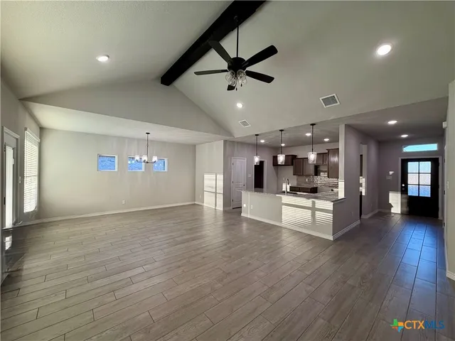a view of an empty room and kitchen with furniture wooden floor and fan