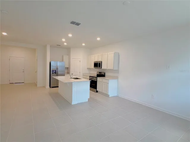 a kitchen with stainless steel appliances kitchen island sink refrigerator and white cabinets