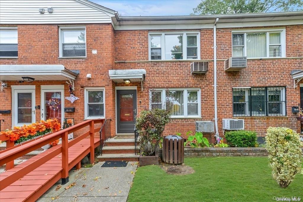 View of front of house with brick siding, a front yard, and a wall unit AC