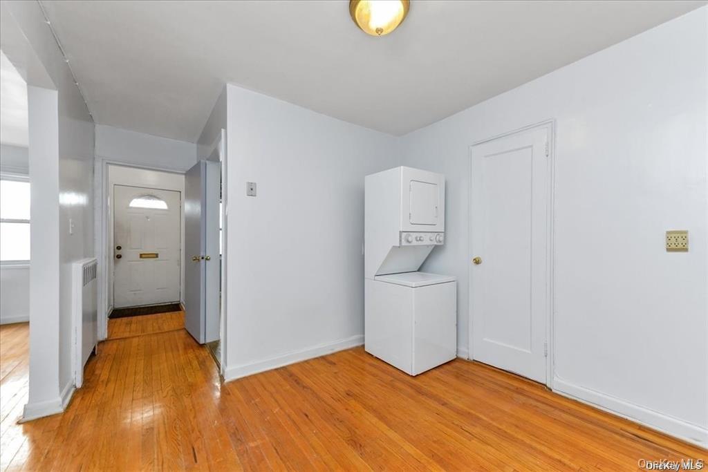 68-02 140th Street, Unit A Queens, NY 11367 - Photo 5 of 16 Laundry area with light wood finished floors, stacked washing machine and dryer, and radiator