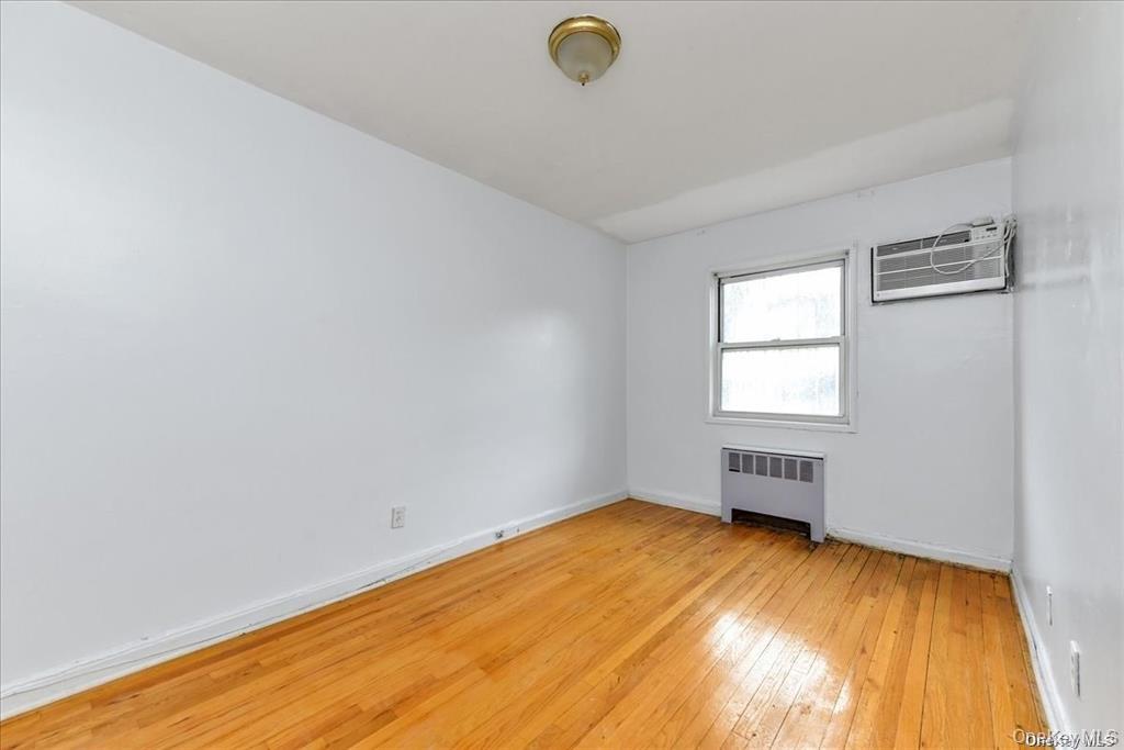 68-02 140th Street, Unit A Queens, NY 11367 - Photo 6 of 16 Unfurnished room featuring light wood-style floors, radiator heating unit, and a wall mounted air conditioner