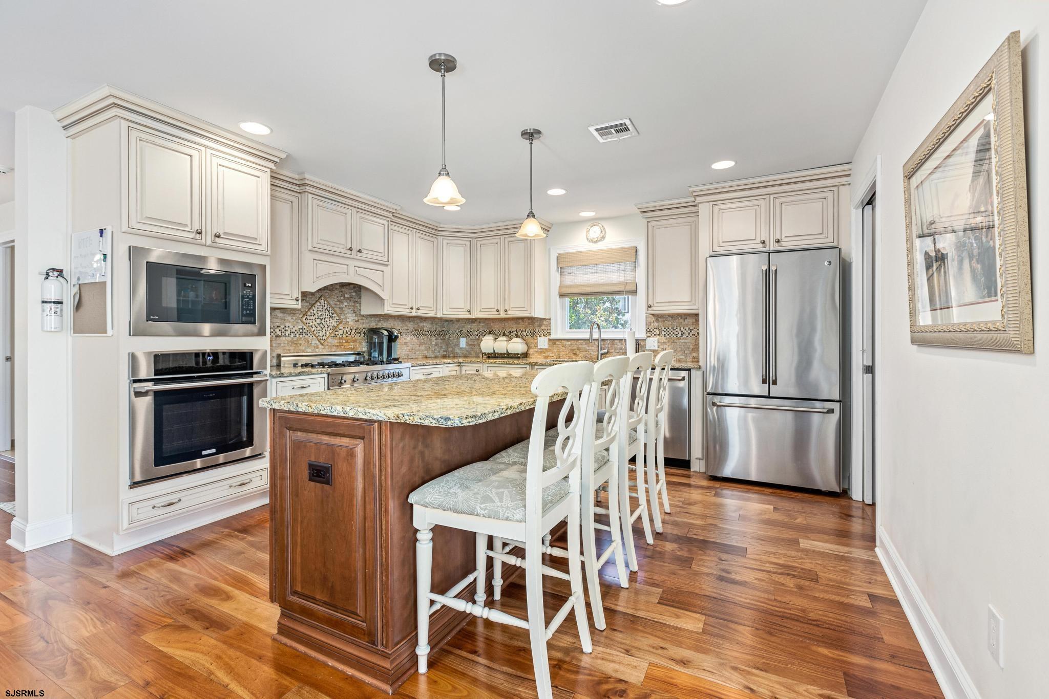 29 North Iroquois Avenue, Unit 6/16/26 FLEXIBLE WITH START DATE Margate City, NJ 08402 - Photo 5 of 40 a kitchen with stainless steel appliances granite countertop a refrigerator a stove a sink a dining table and chairs with wooden floor