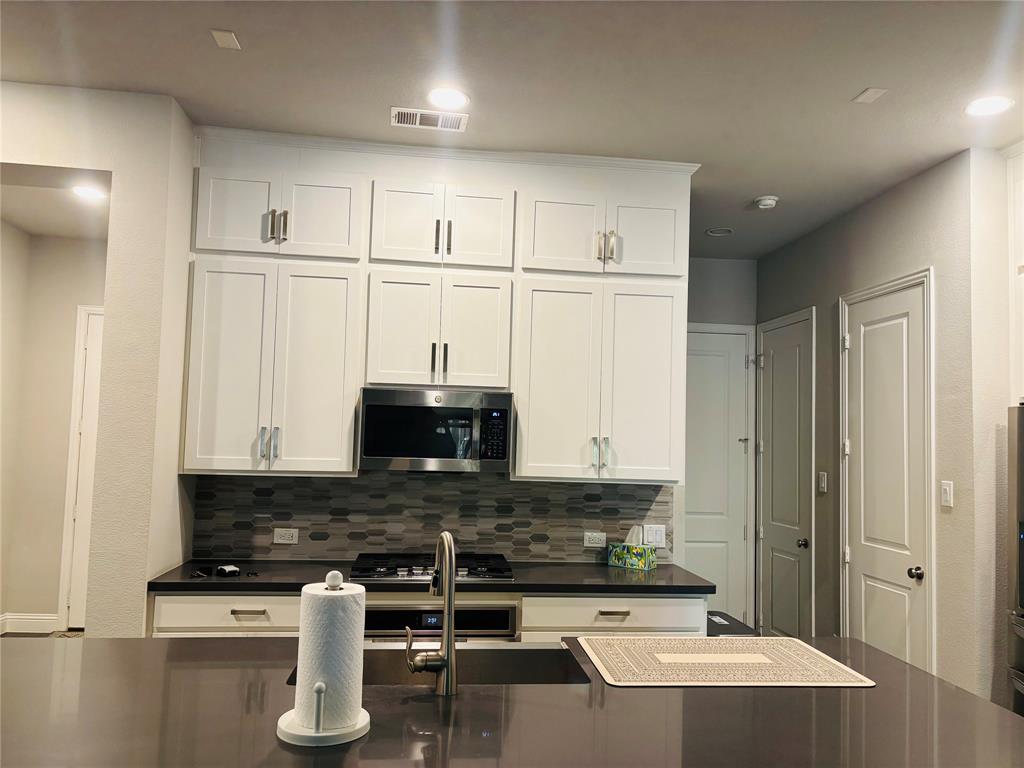 8223 Snapdragon Way Dallas, TX 75252 - Photo 16 of 32 Kitchen featuring white cabinets, decorative backsplash, and stainless steel microwave