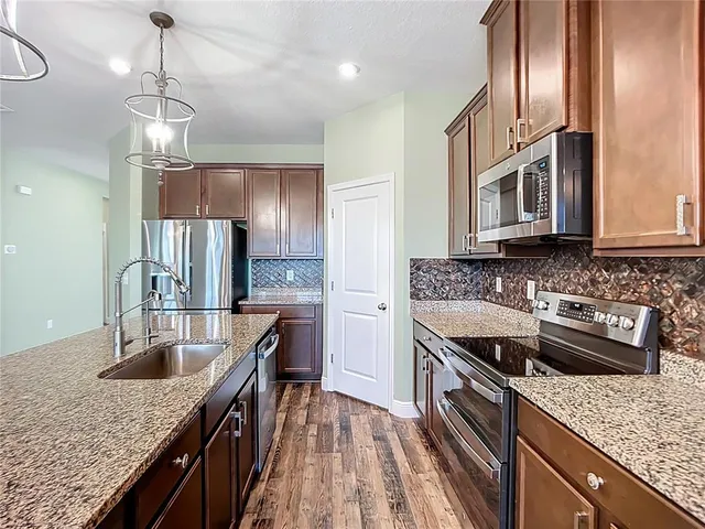 a kitchen with stainless steel appliances kitchen island granite countertop a refrigerator a stove and a sink