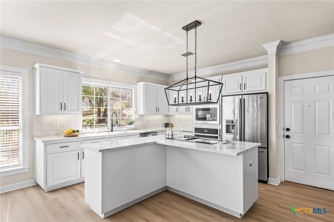 5901 Round Table Cove Austin, TX 78746 - Photo 16 of 46 a kitchen with stainless steel appliances a sink a stove a refrigerator cabinets and wooden floor