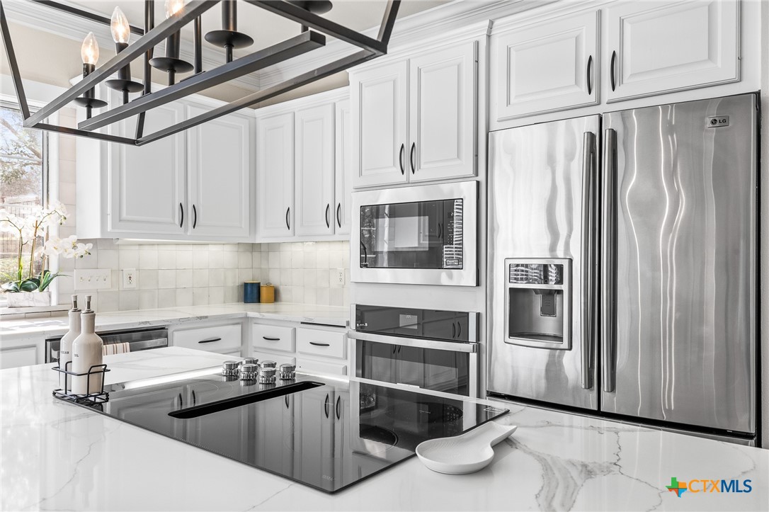 5901 Round Table Cove Austin, TX 78746 - Photo 20 of 46 a kitchen with stainless steel appliances a refrigerator a sink and wooden cabinets