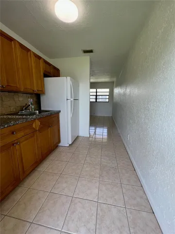 a view of a refrigerator in kitchen and an empty room in wooden floor