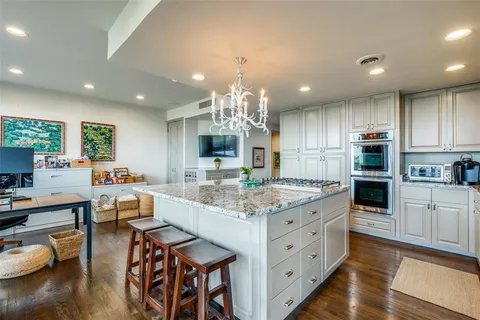 a kitchen with stainless steel appliances kitchen island granite countertop a stove top oven a sink dishwasher and white cabinets with wooden floor