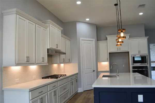 a kitchen with kitchen island granite countertop a stove a sink dishwasher and a microwave oven with white cabinets