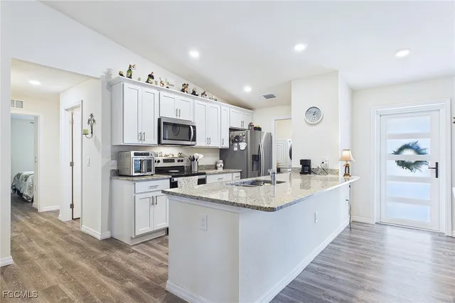 a large kitchen with stainless steel appliances granite countertop a stove top oven a refrigerator a sink and dishwasher with wooden floor