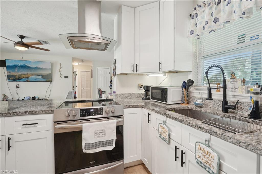 501 Penn Road West Lehigh Acres, FL 33936 - Photo 20 of 27 a kitchen with stainless steel appliances granite countertop a stove a sink dishwasher and white cabinets with wooden floor