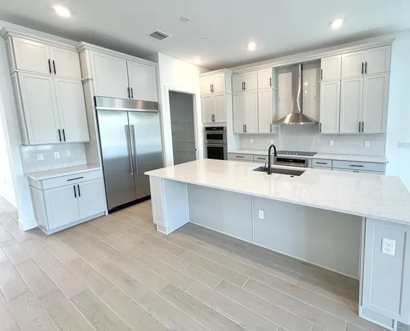 a large kitchen with stainless steel appliances a large counter top a sink a refrigerator and white cabinets