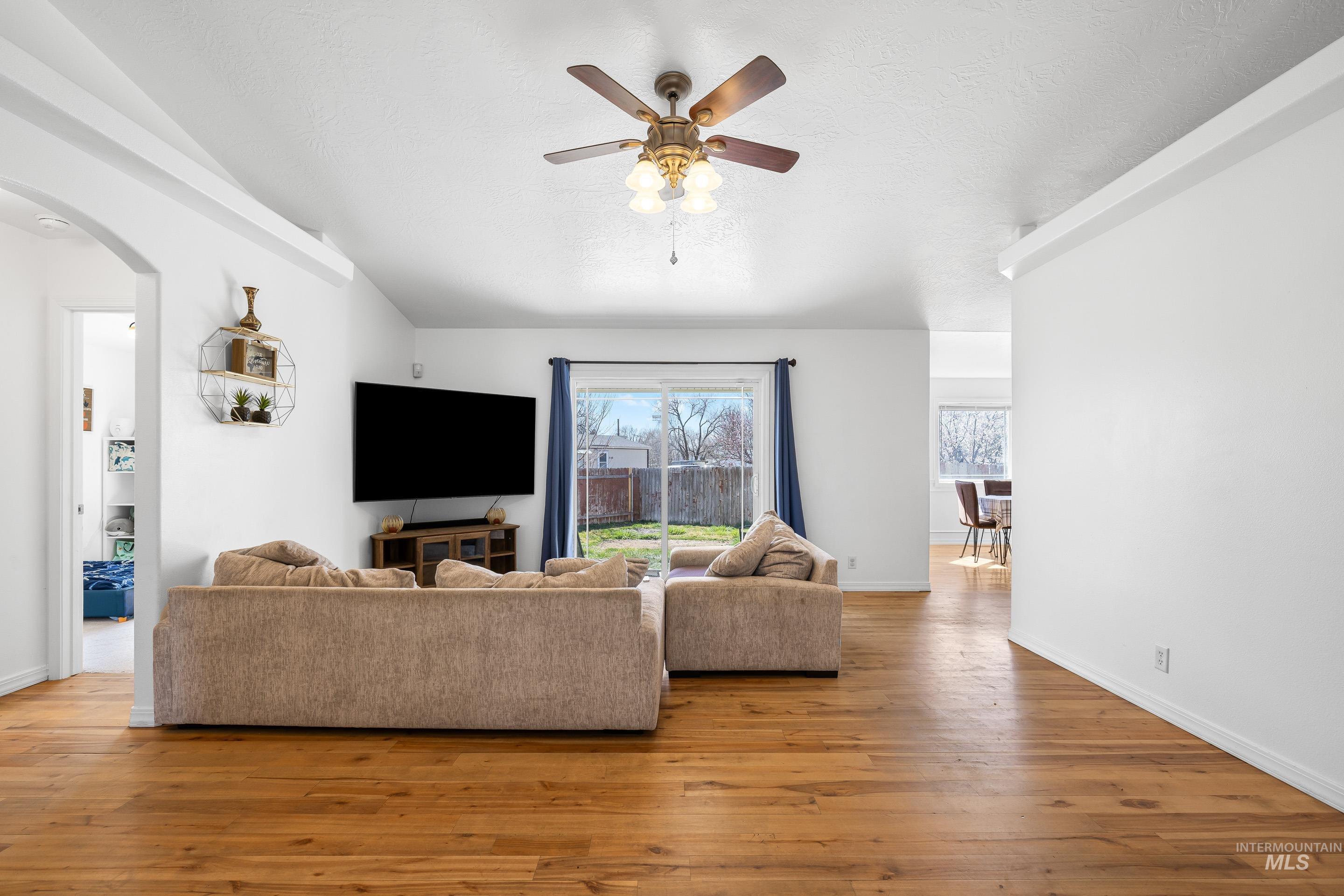 215 Northeast Rosa Court Mountain Home, ID 83647 - Photo 11 of 39 Living area with arched walkways, light wood finished floors, ceiling fan, and a textured ceiling