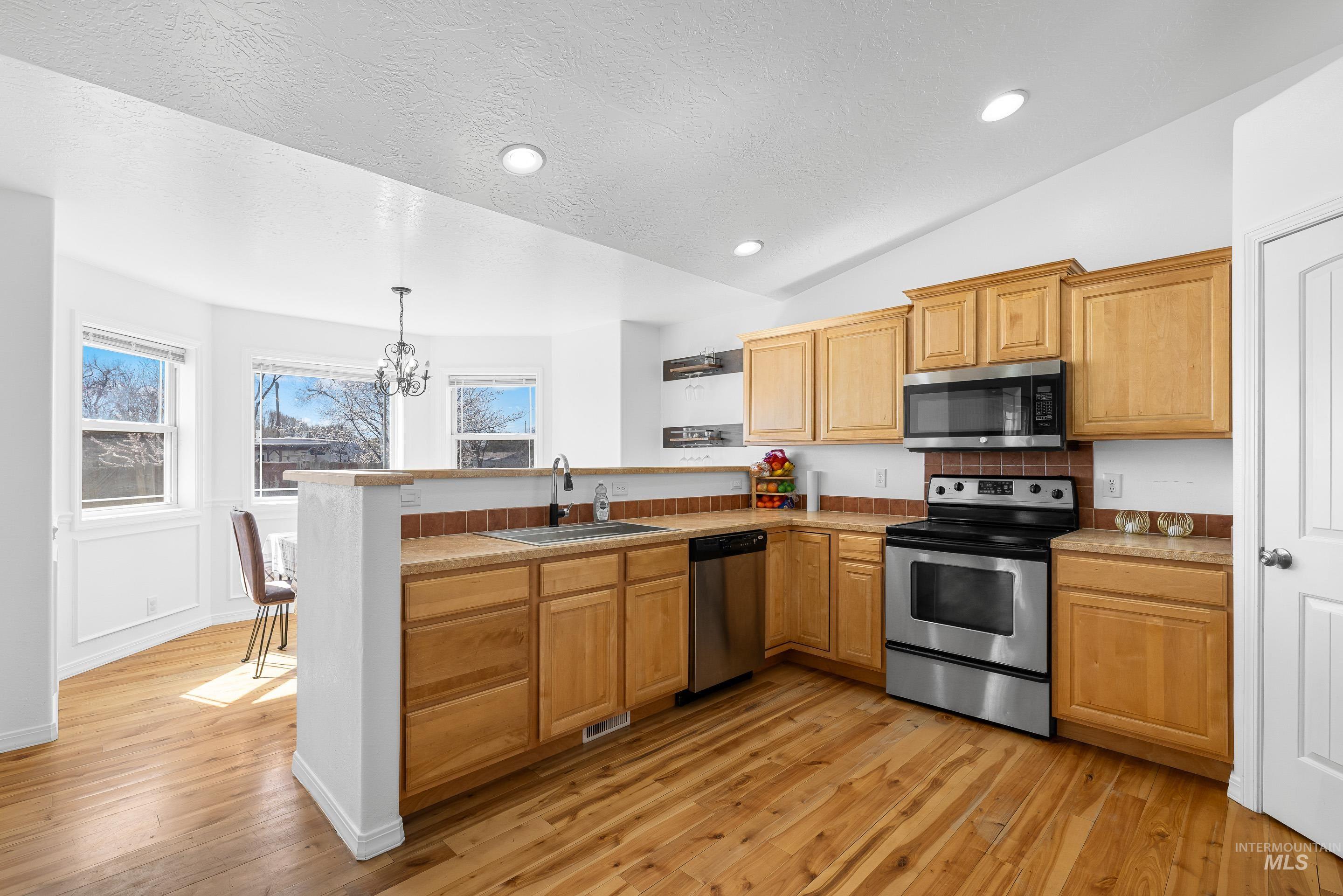 215 Northeast Rosa Court Mountain Home, ID 83647 - Photo 12 of 39 Kitchen featuring a peninsula, stainless steel appliances, light countertops, suspended lighting, and light wood-type flooring