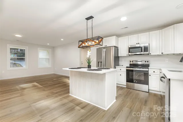 a kitchen with granite countertop a stove a sink dishwasher a refrigerator and a dining table with wooden floor