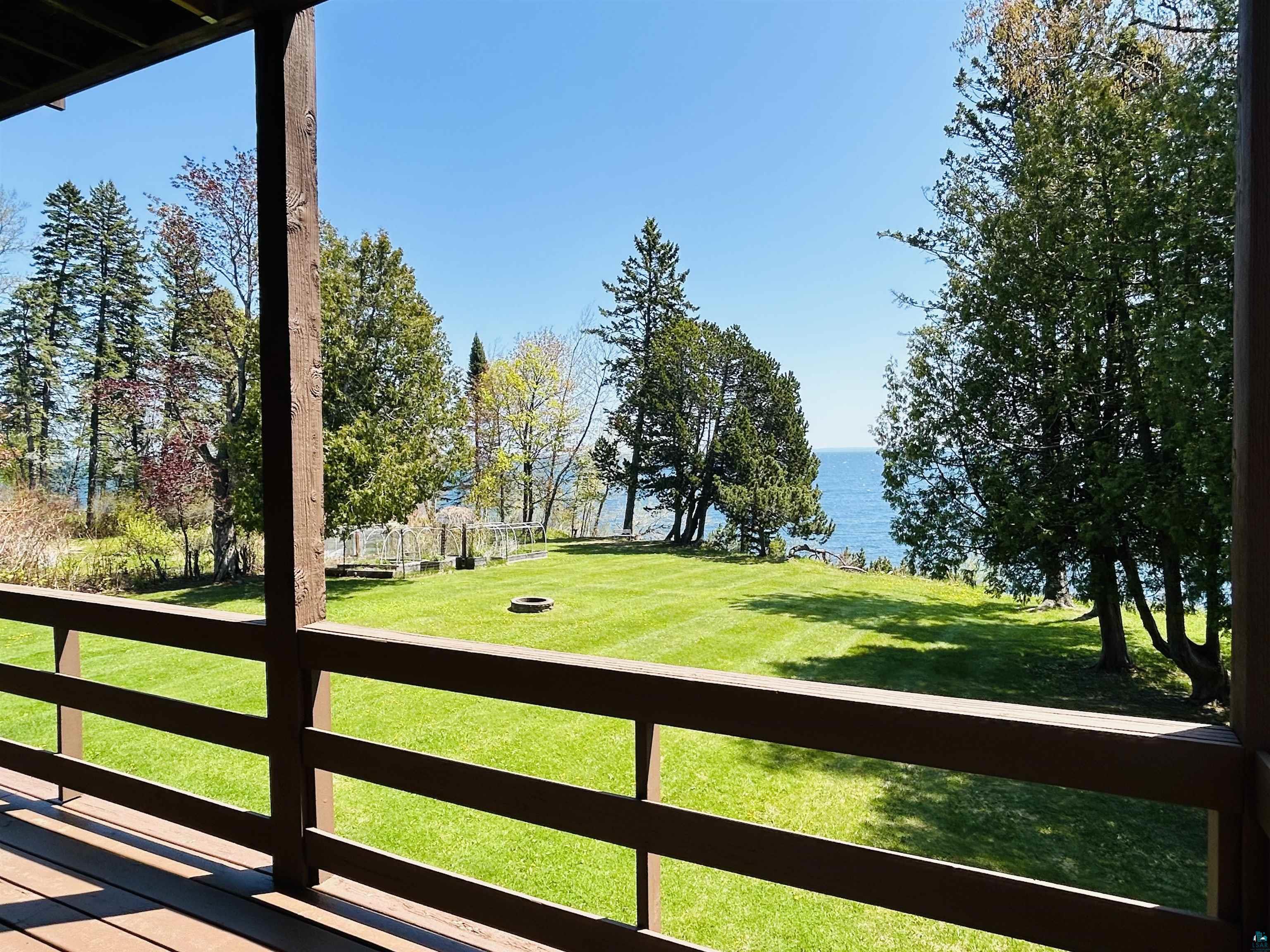 5090 London Road, Unit 1 Duluth, MN 55804 - Photo 36 of 54 Spacious outdoor deck with a wooden railing system overlooking a manicured lawn, mature trees, and a substantial body of water