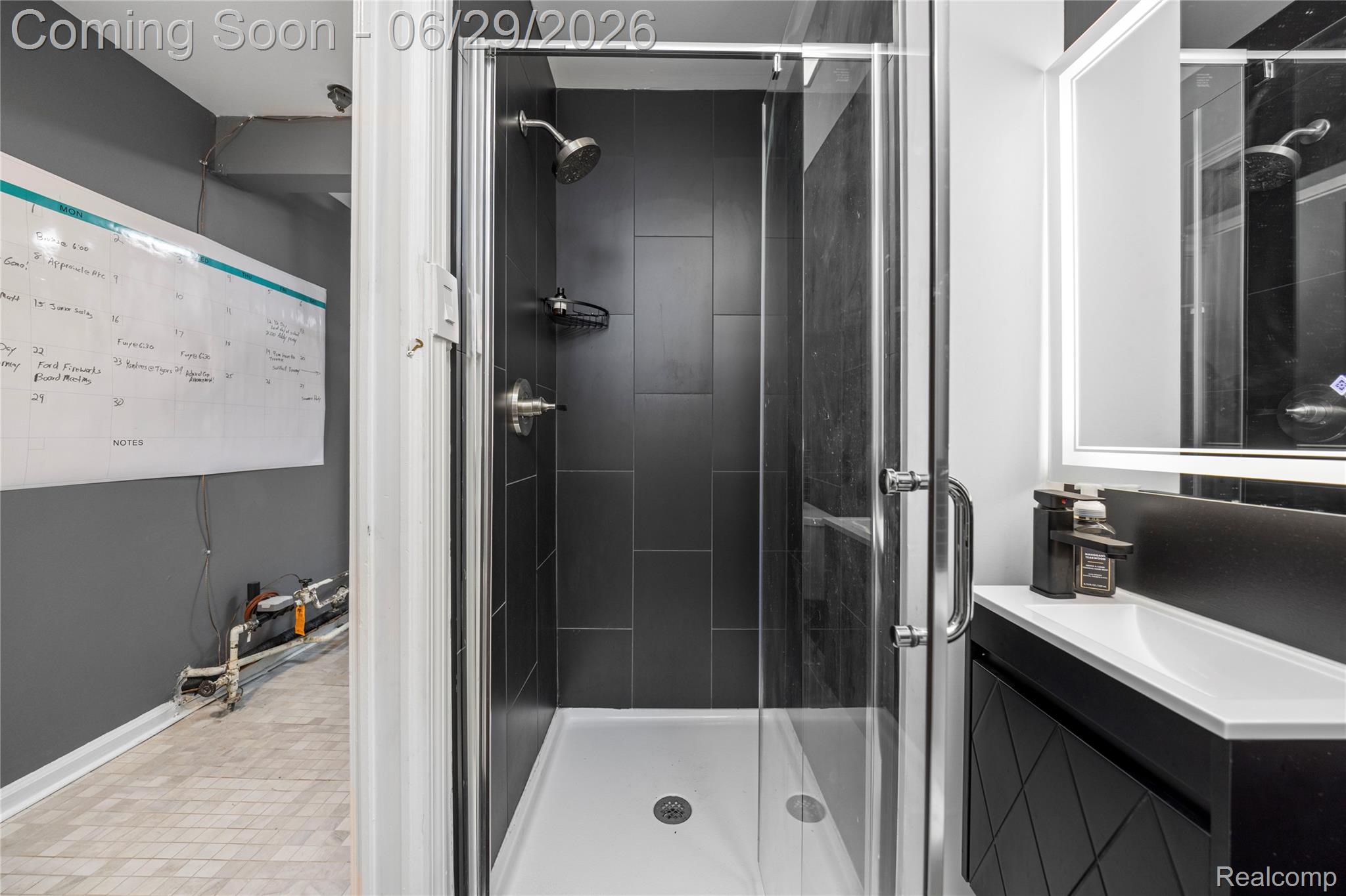 6085 Worlington Road Bloomfield Hills, MI 48301 - Photo 46 of 75 Contemporary bathroom featuring a glass-enclosed shower with dark tile surround, wall-mounted vanity with integrated sink, and an illuminated mirror
