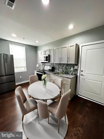 a kitchen with stainless steel appliances granite countertop a dining table chairs refrigerator and sink