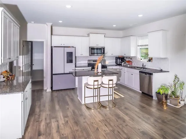 a kitchen with stainless steel appliances granite countertop a refrigerator a stove top oven a sink dishwasher and white cabinets with wooden floor