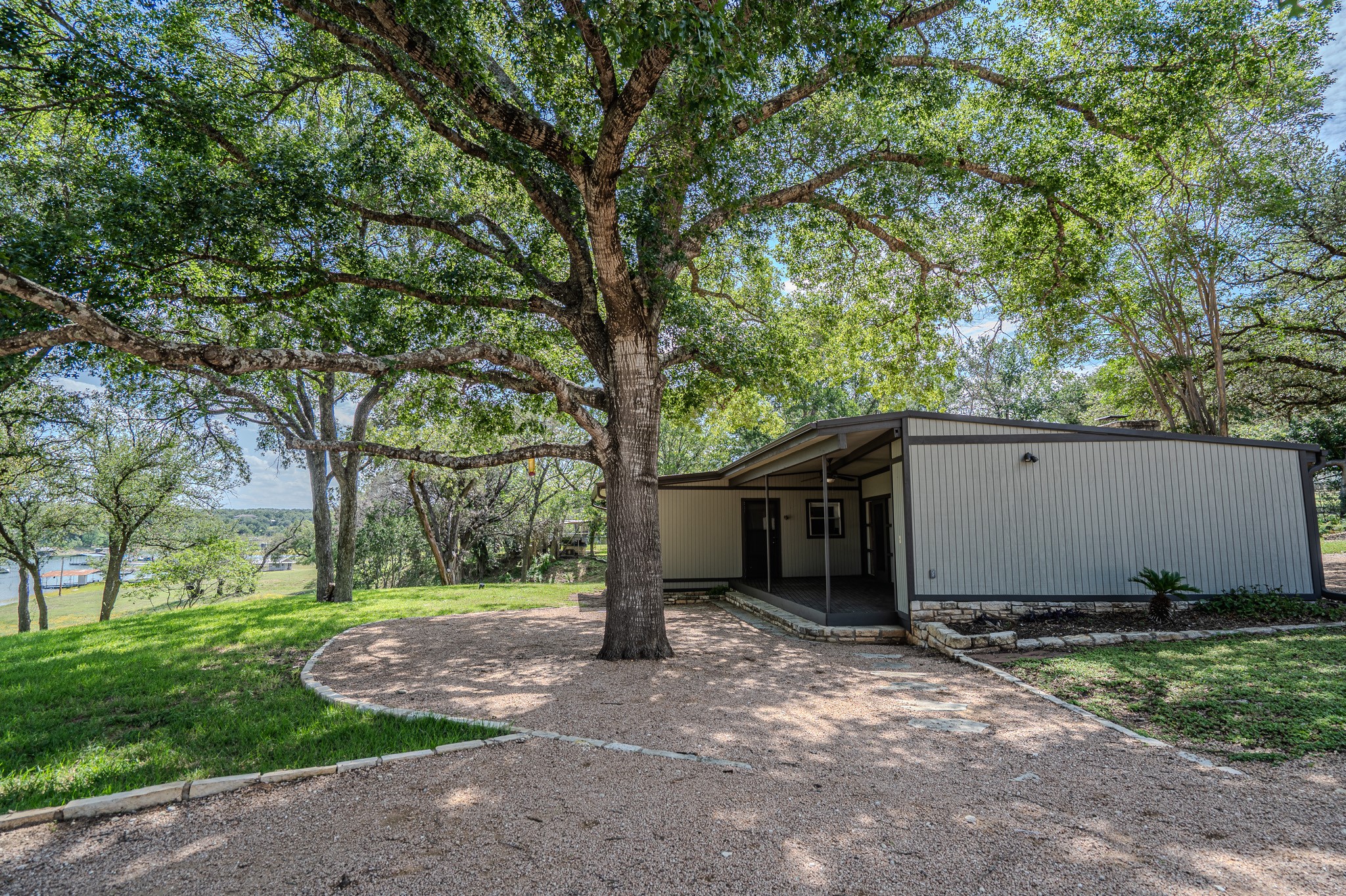 16013 Edwards Drive Austin, TX 78734 - Photo 2 of 18 Mature trees shade a charming residence, featuring a covered porch and gravel driveway.