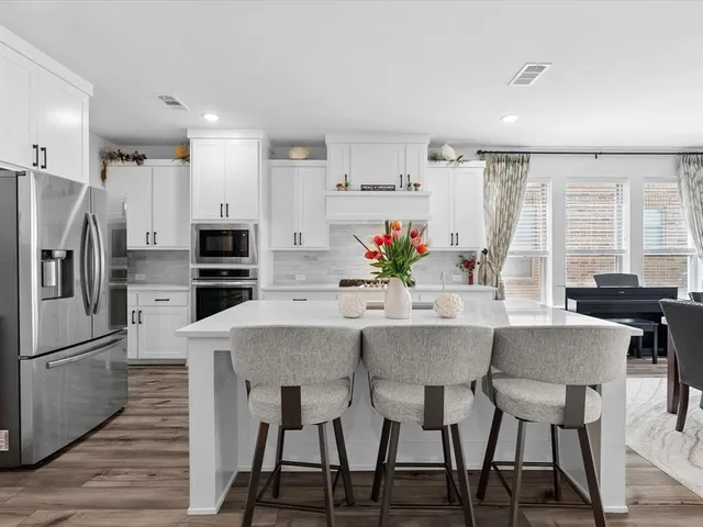a kitchen with stainless steel appliances a dining table chairs refrigerator and sink