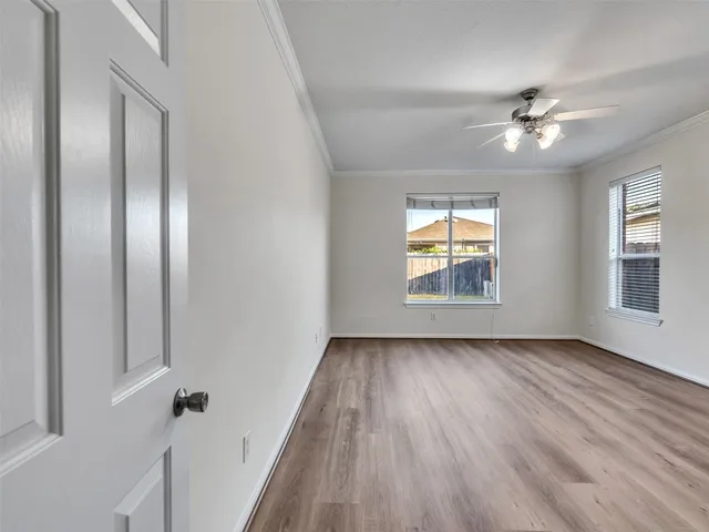 an empty room with wooden floor chandelier fan and windows