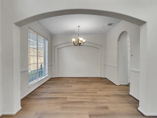 an empty room with wooden floor chandelier and windows