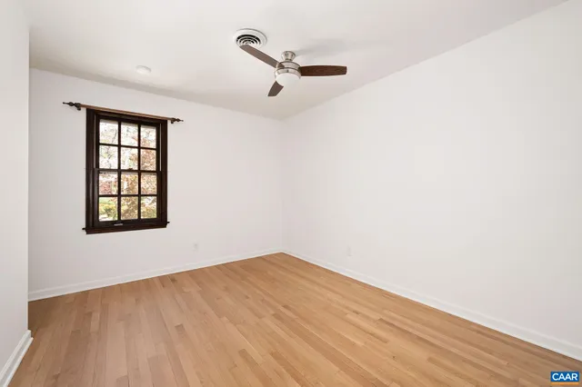 an empty room with wooden floor fan and windows