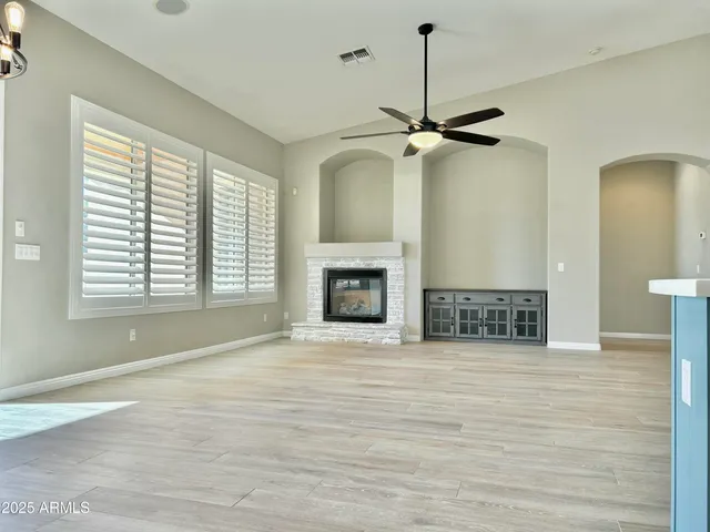 a view of a room with a fireplace a ceiling fan and wooden floor