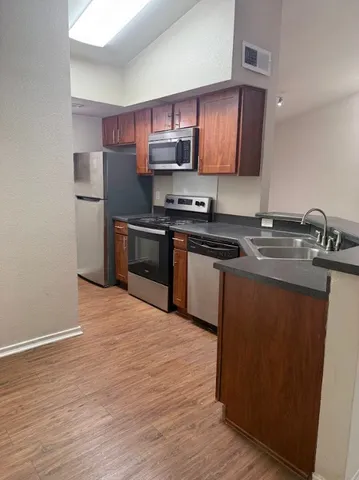 a kitchen with stainless steel appliances granite countertop a stove top oven a sink and dishwasher a refrigerator with wooden floor