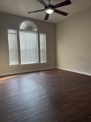 an empty room with wooden floor fan and windows