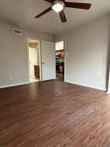 an empty room with wooden floor chandelier fan and windows