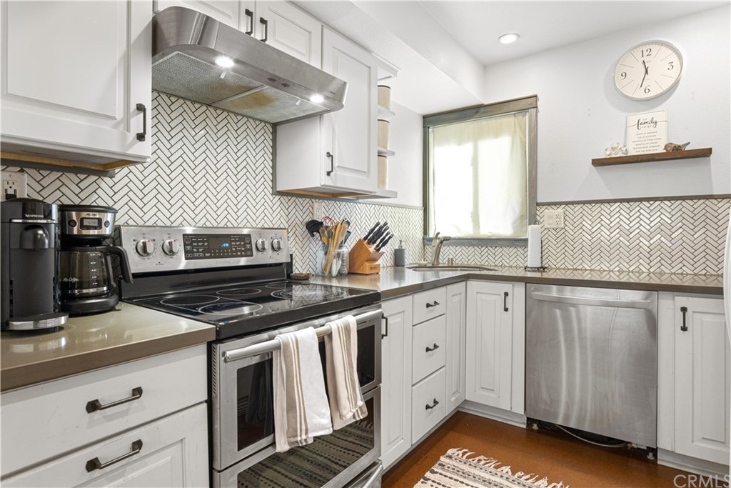a kitchen with granite countertop a stove a sink dishwasher and white cabinets with wooden floor