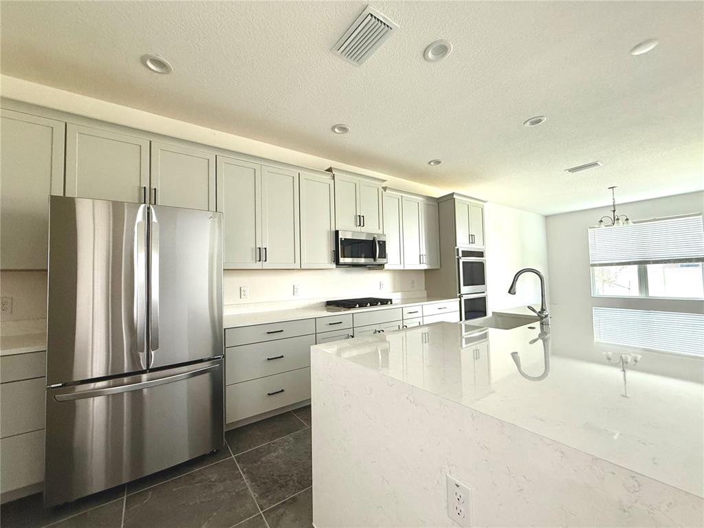 394 Switchgrass Loop Minneola, FL 34715 - Photo 9 of 26 a kitchen with stainless steel appliances granite countertop a refrigerator a stove a sink dishwasher and white cabinets with wooden floor