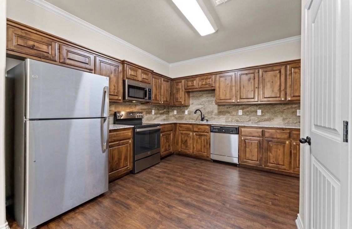 113 Calvin Smith Ln. Lane Jarrell, TX 76537 - Photo 5 of 16 a kitchen with granite countertop wooden floors stainless steel appliances and a counter space