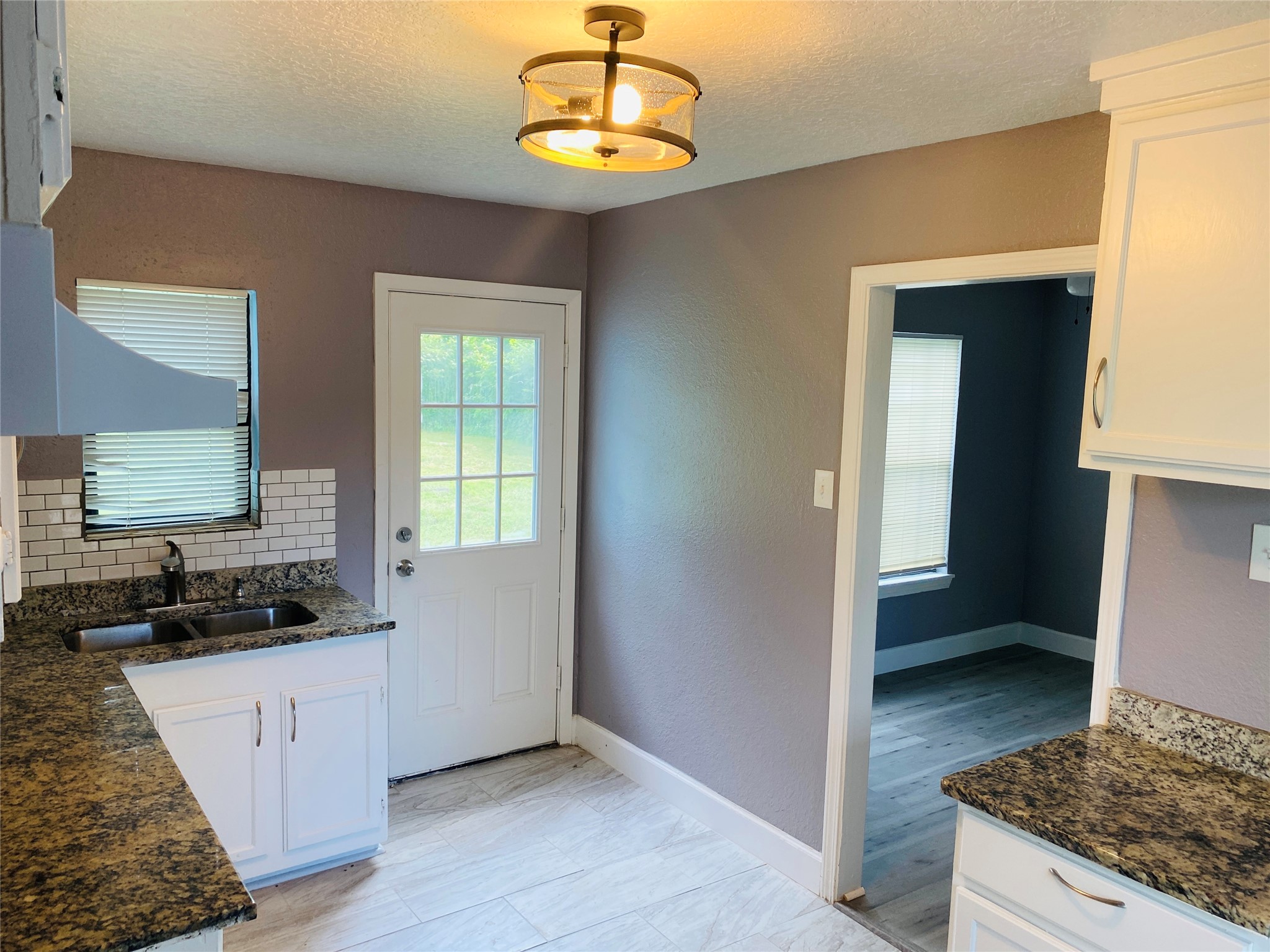 7547 Laura Koppe Road Houston, TX 77028 - Photo 6 of 11 This kitchen features modern granite countertops, white cabinetry, and a stylish backsplash. It has a cozy layout with a window and door providing natural light, and opens to an adjacent room with wood flooring.